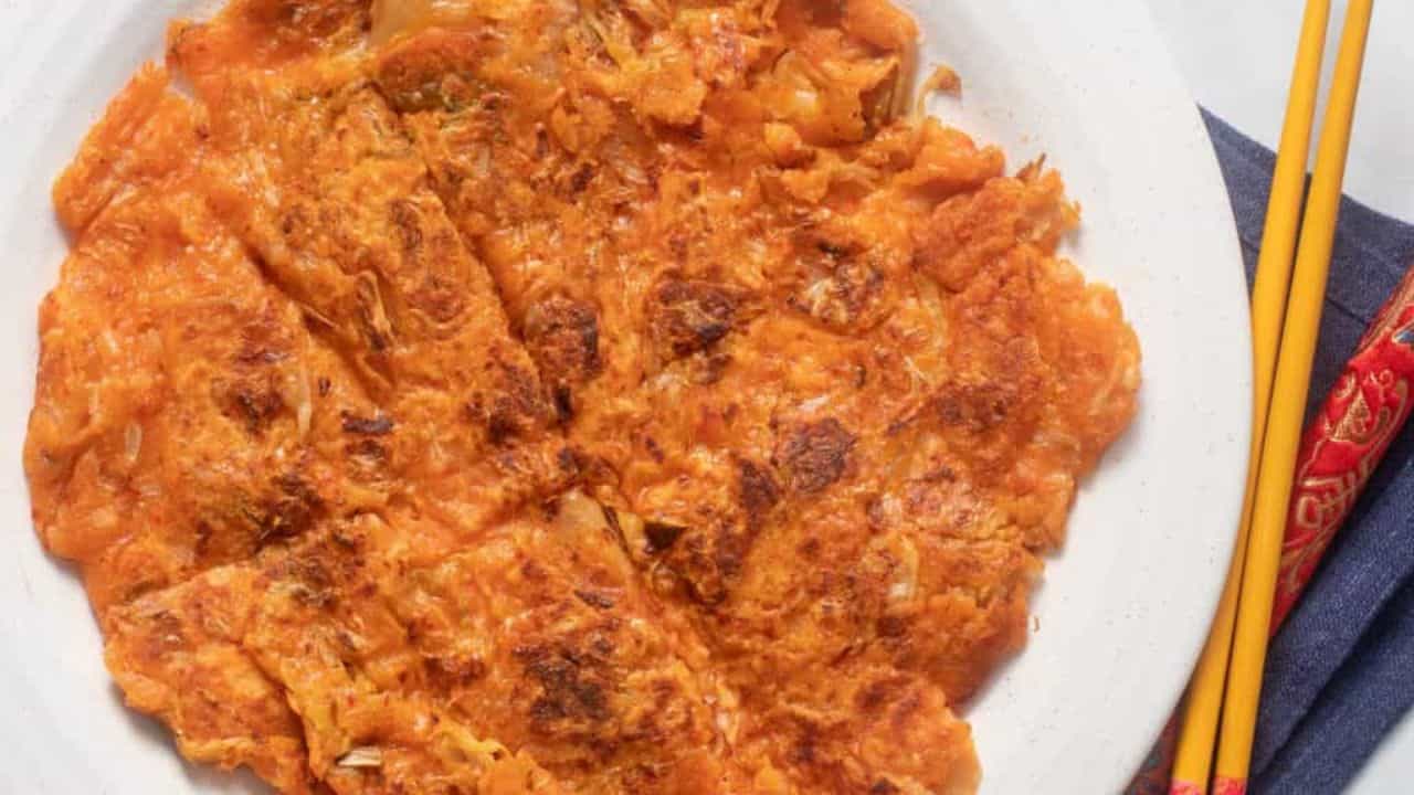 A close-up image of kimchi pancake on a white plate with chopsticks beside it.
