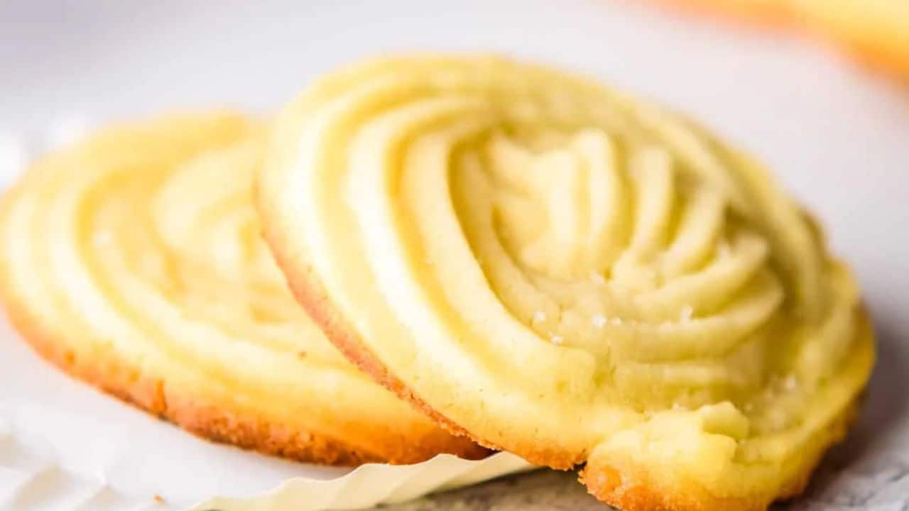 Four swirled butter cookies, each nestled in a white paper liner, arranged on a wooden tray.