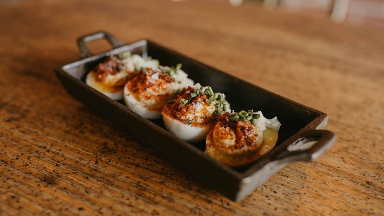 A rectangular dish with four deviled eggs topped with paprika, chopped green onions, and a side of chopped lettuce, placed on a wooden surface.