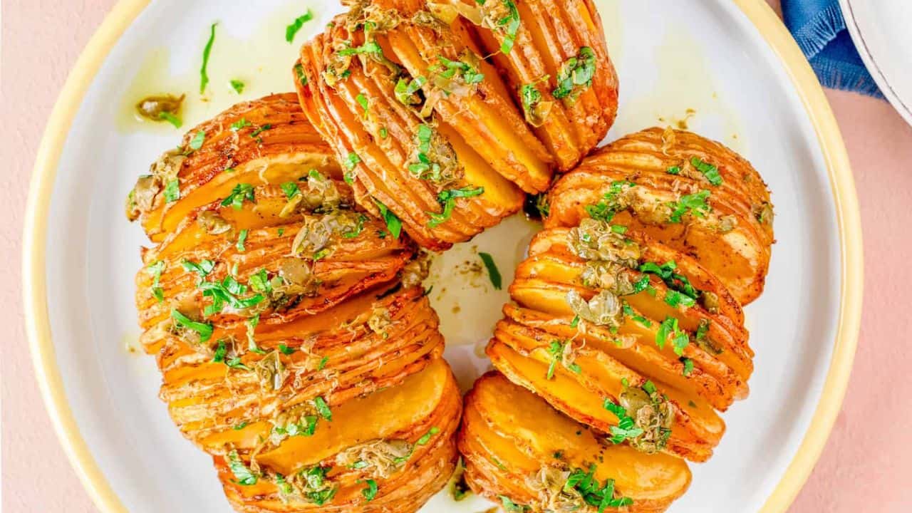An overhead image of air fried hassel back potatoes on a plate with parsley on top and a fork and knife on the right side.