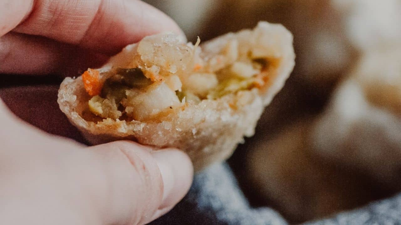 A hand holds a half-eaten fried dumpling, revealing a filling of mixed vegetables.