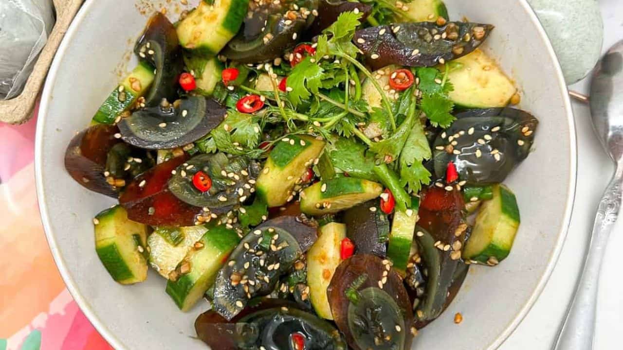 Unique and flavorful century egg salad paired with crisp cucumber in a white bowl.