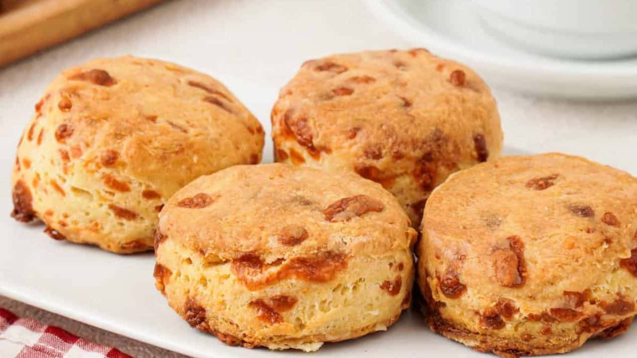 Close-up of four flaky buttermilk cheddar cheese biscuits arranged on a white plate.