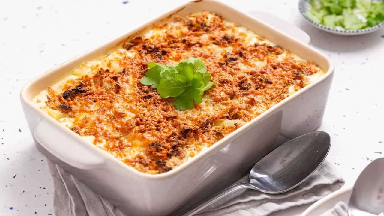 A close up image of cheesy potatoes in a casserole, garnished with parsley.
