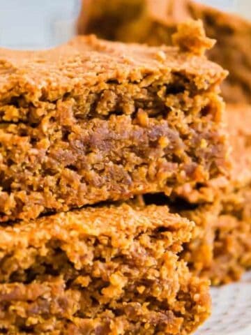 A close-up of three square pieces of moist, golden-brown baked bars stacked on a white plate.