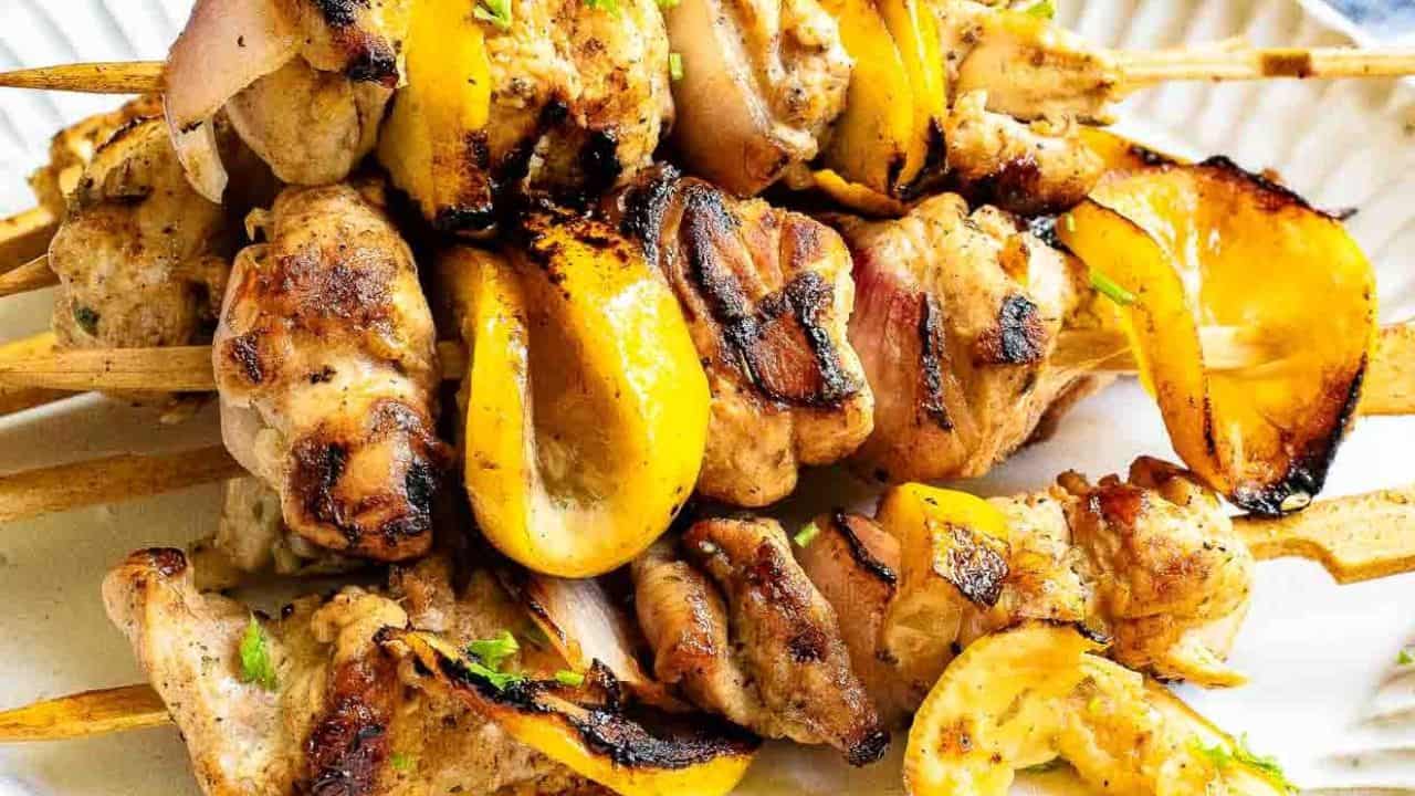 Grilled Greek lemon chicken kabobs with herbs and lemon slices.