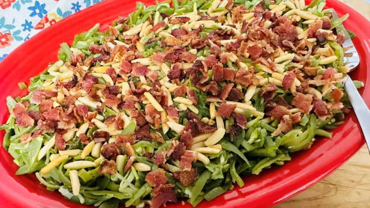 Green beans with bacon and almonds on a red plate.