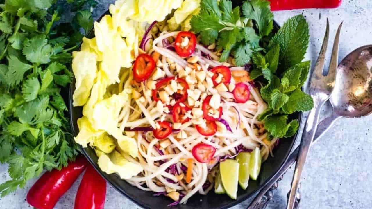 Overhead shot of green papaya salad in a black bowl.