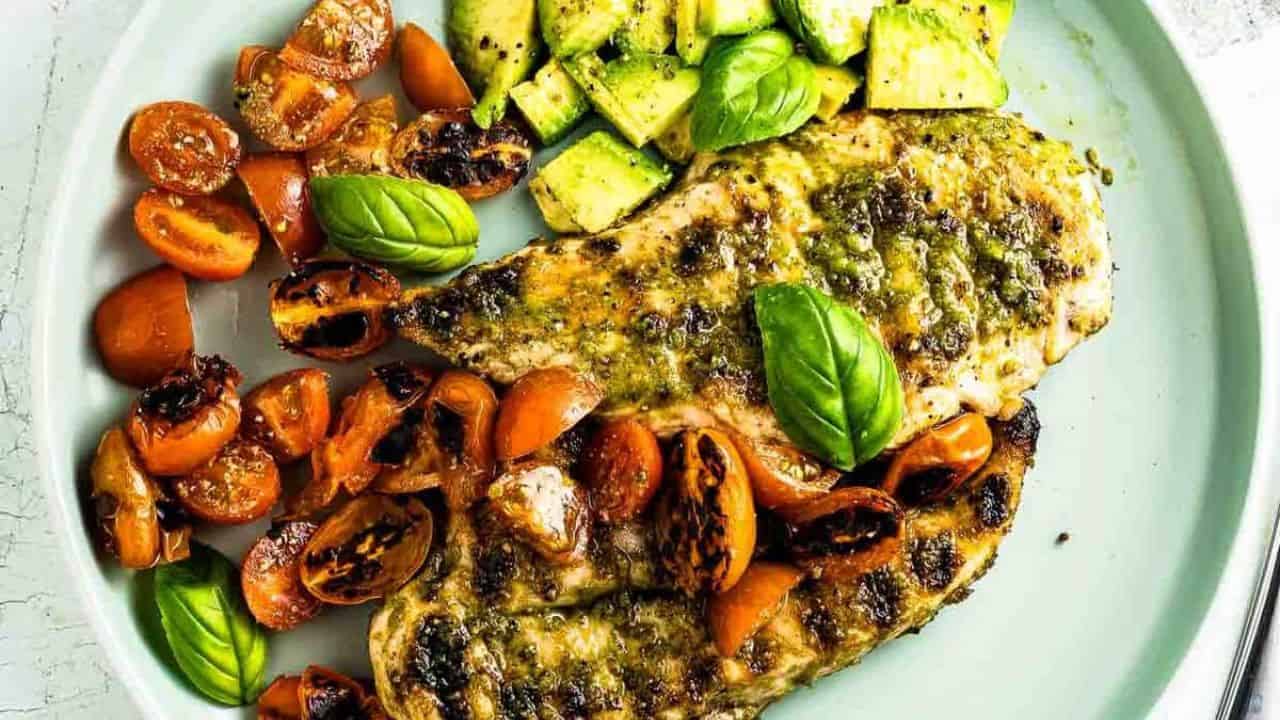 Plate of basil pesto chicken with grilled tomatoes and avocado slices.