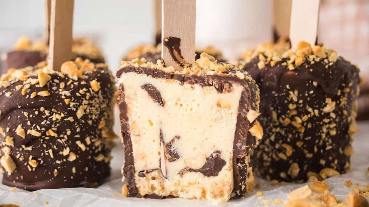Ice cream bars coated in chocolate and crushed nuts, with one bar cut in half to show the creamy interior and chocolate swirls.