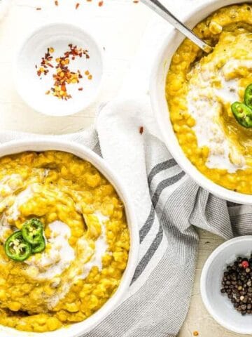 Two bowls of lentil soup garnished with sliced green chili and a swirl of cream, placed on a striped towel alongside seasonings and olive oil.