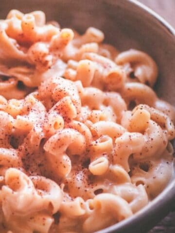 A bowl of macaroni and cheese topped with ground black pepper, with a fork resting inside the bowl.