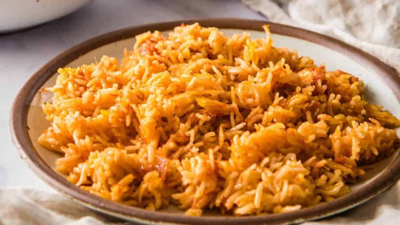 A close-up of a pot with cooked jollof rice with a person's hand holding a red spatula.