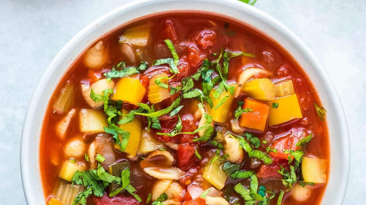 Olive Garden Minestrone Soup in a white bowl topped with basil.