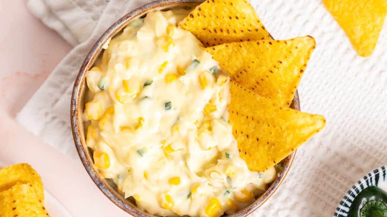 An image of jalapeno corn in a wooden bowl with tortilla chips on the side.