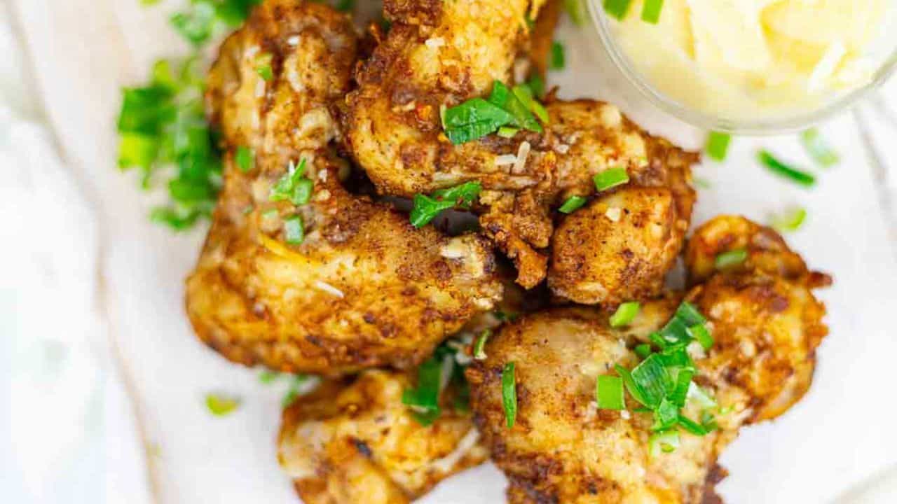 A plate of seasoned, cooked chicken drumsticks garnished with chopped green herbs, served next to a small bowl of dipping sauce.