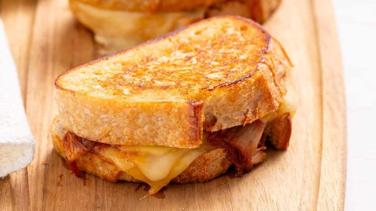 A grilled cheese sandwich with melted cheese and pulled meat is placed on a wooden board.