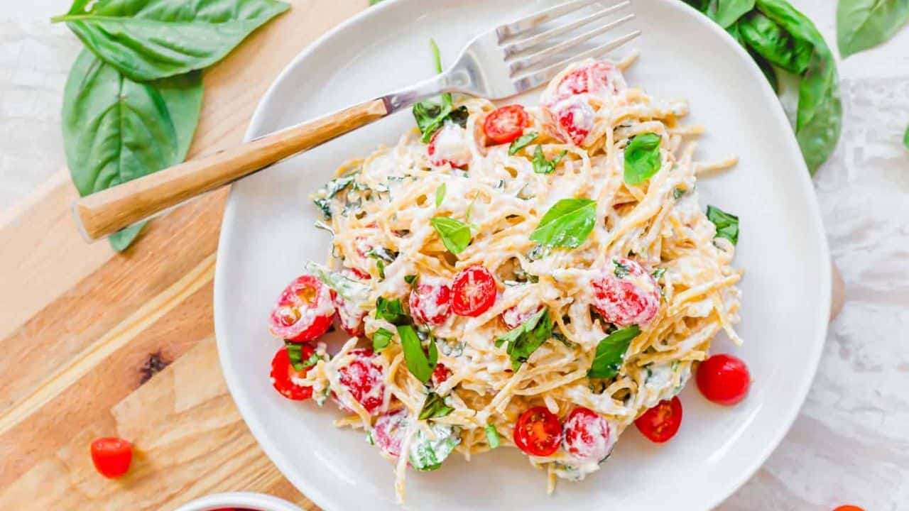 Lemon ricotta pasta with cherry tomatoes and basil on a white plate.