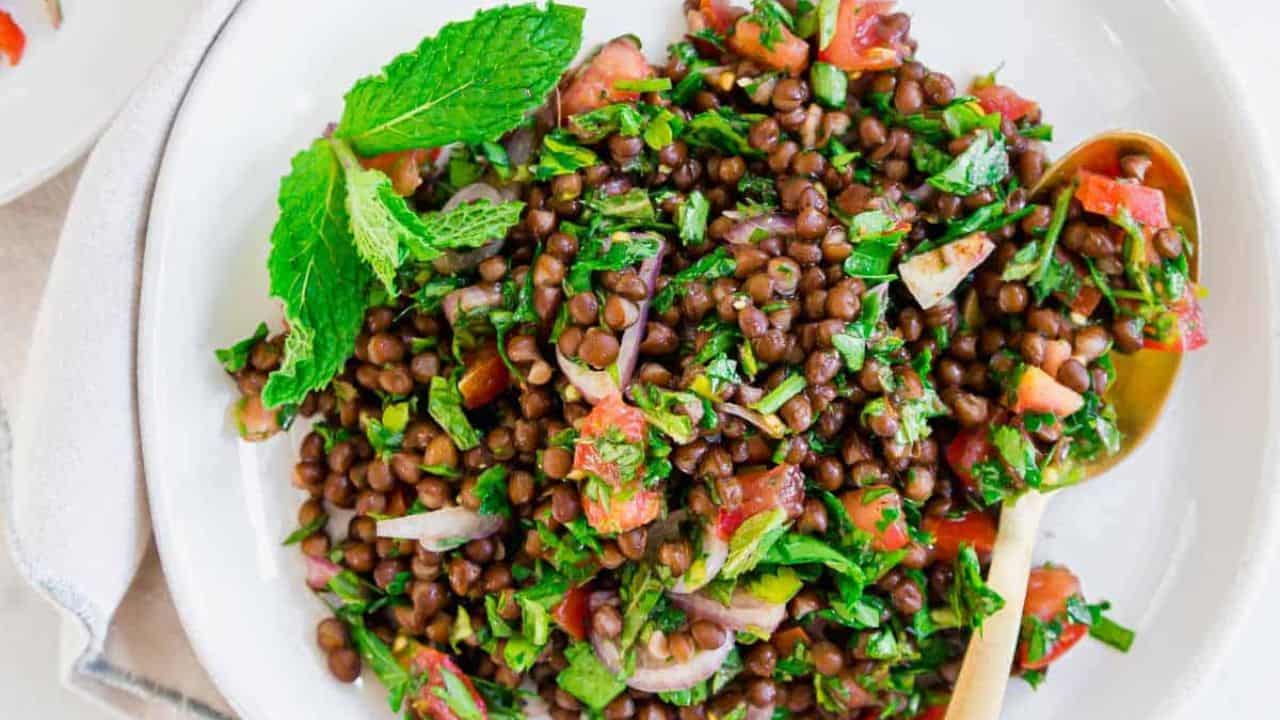 Lentil tabbouleh on a white plate with mint garnish and gold spoon.