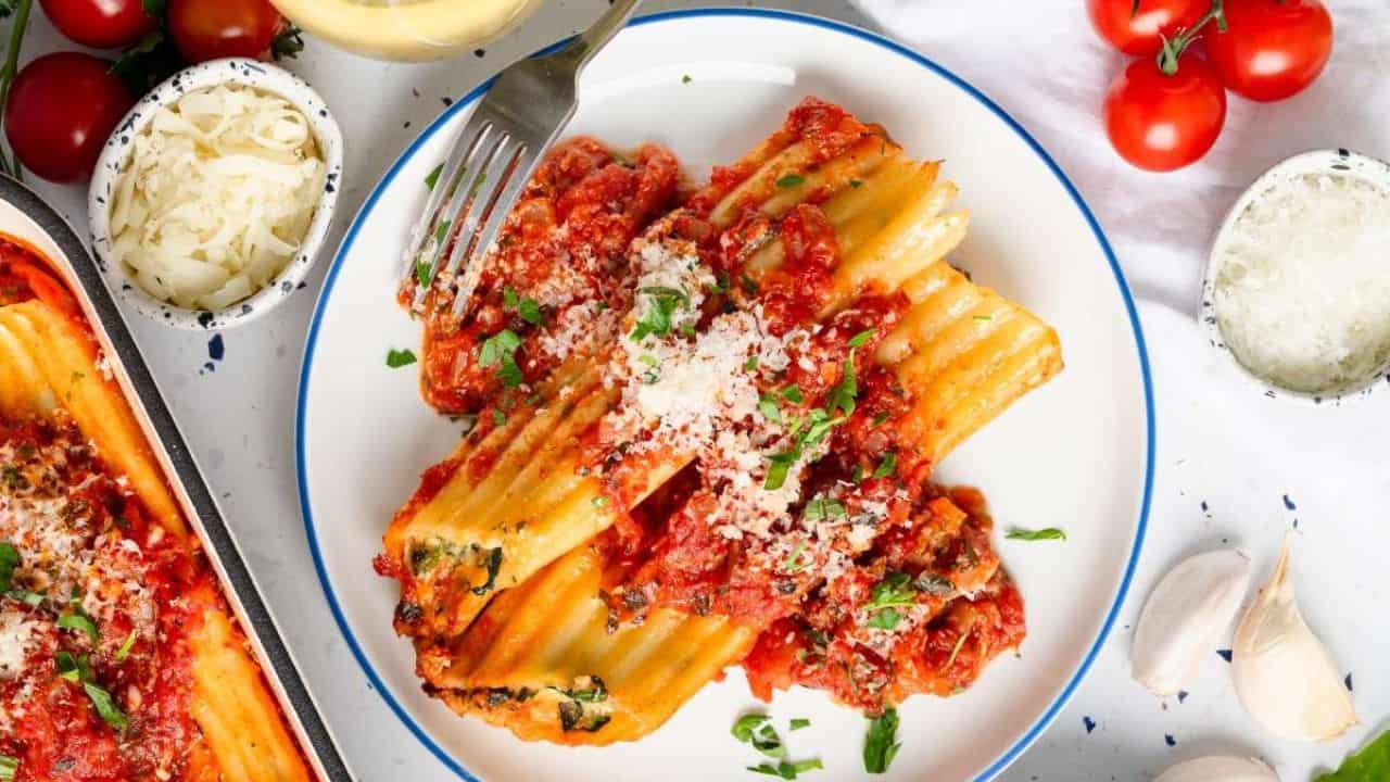 A plate of pasta topped with tomato sauce, grated cheese, and herbs, surrounded by cherry tomatoes, garlic, and bowls of grated cheese.