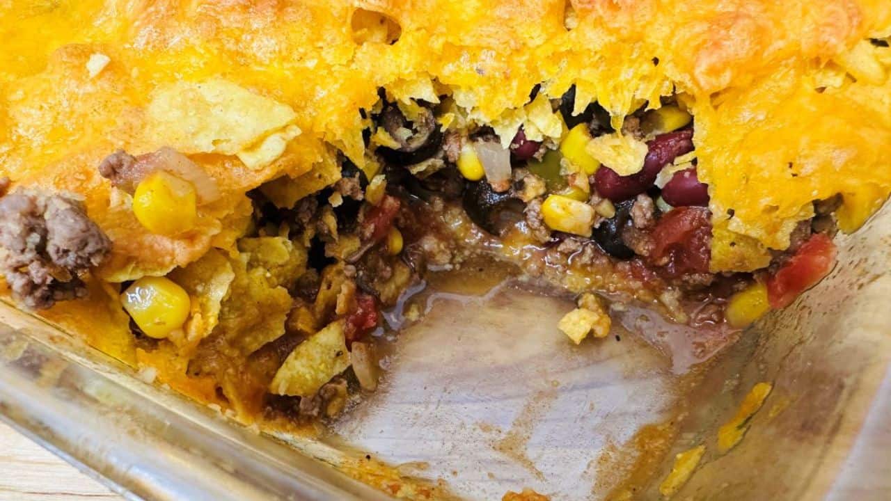 A partially served Mexican casserole in a baking dish, showing layers of corn, beans, cheese, and ground meat.