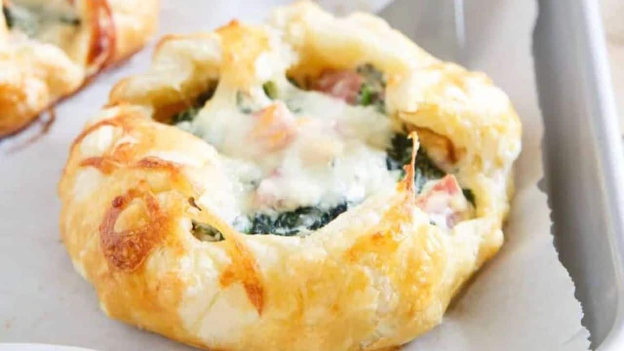 Mini ham and cheese spinach breakfast pies on a baking sheet.