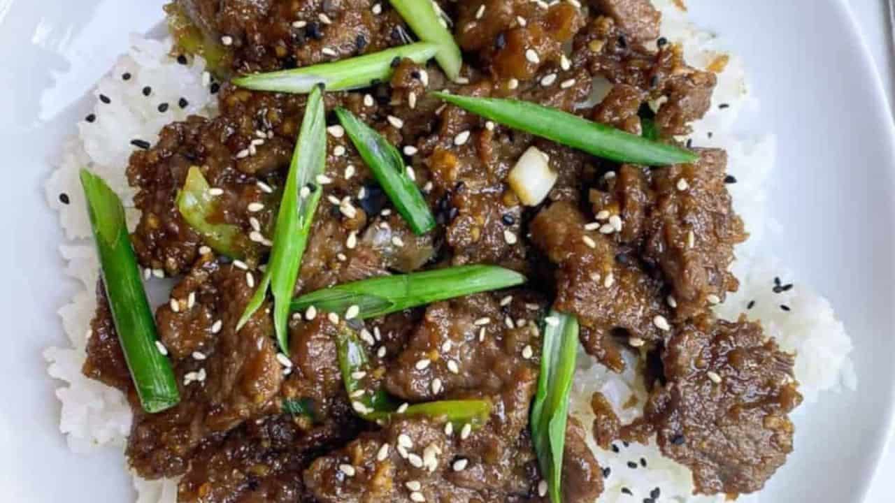 Tender beef stir-fried in a savory and sweet Mongolian-style sauce on top of rice on a plate.