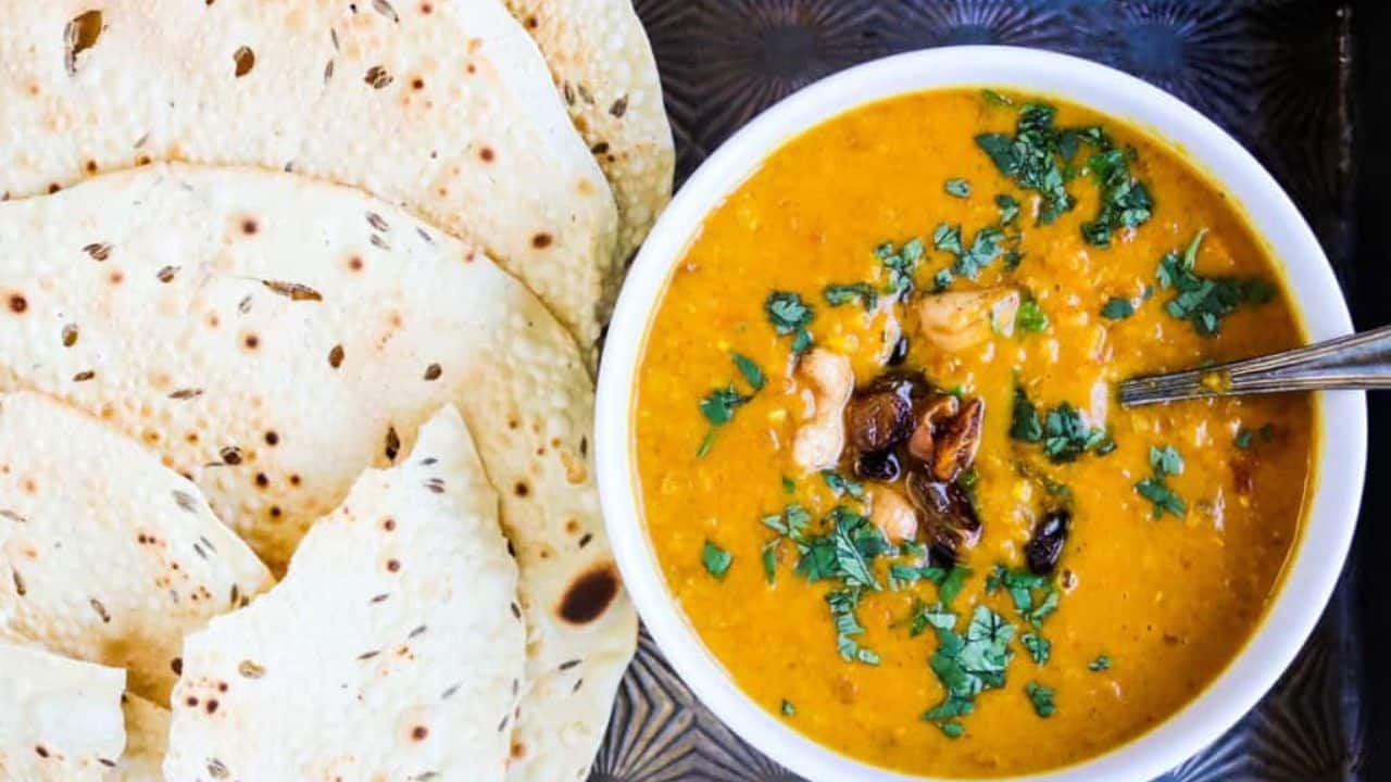 Bowl of mulligatawny soup with a hand lifting a spoonful of soup.