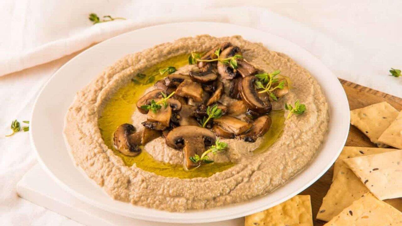 Hummus with mushrooms and crackers on a white plate.