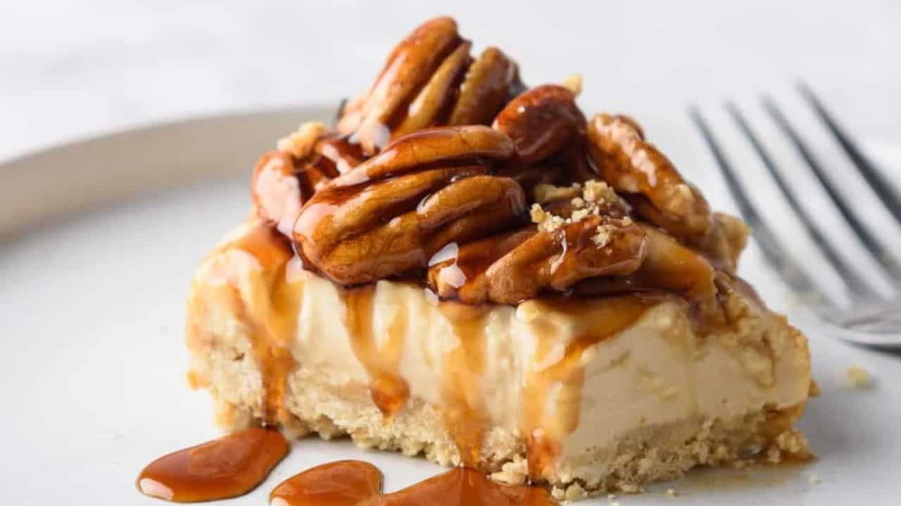 A close up view of pecan pie cheesecake slice on a white plate, with a fork on the side.