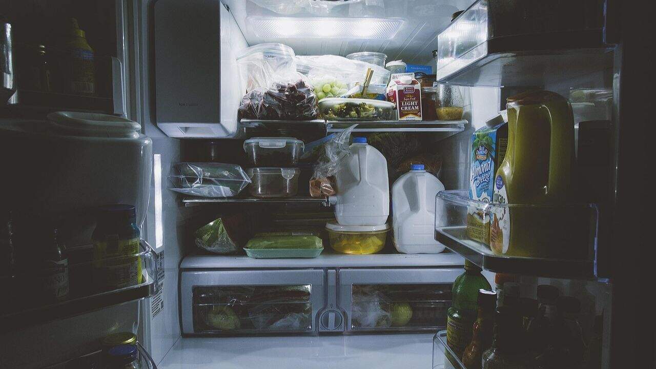 An open refrigerator stocked with various food items including milk, juice, grapes, eggs, condiments, and containers of leftovers.
