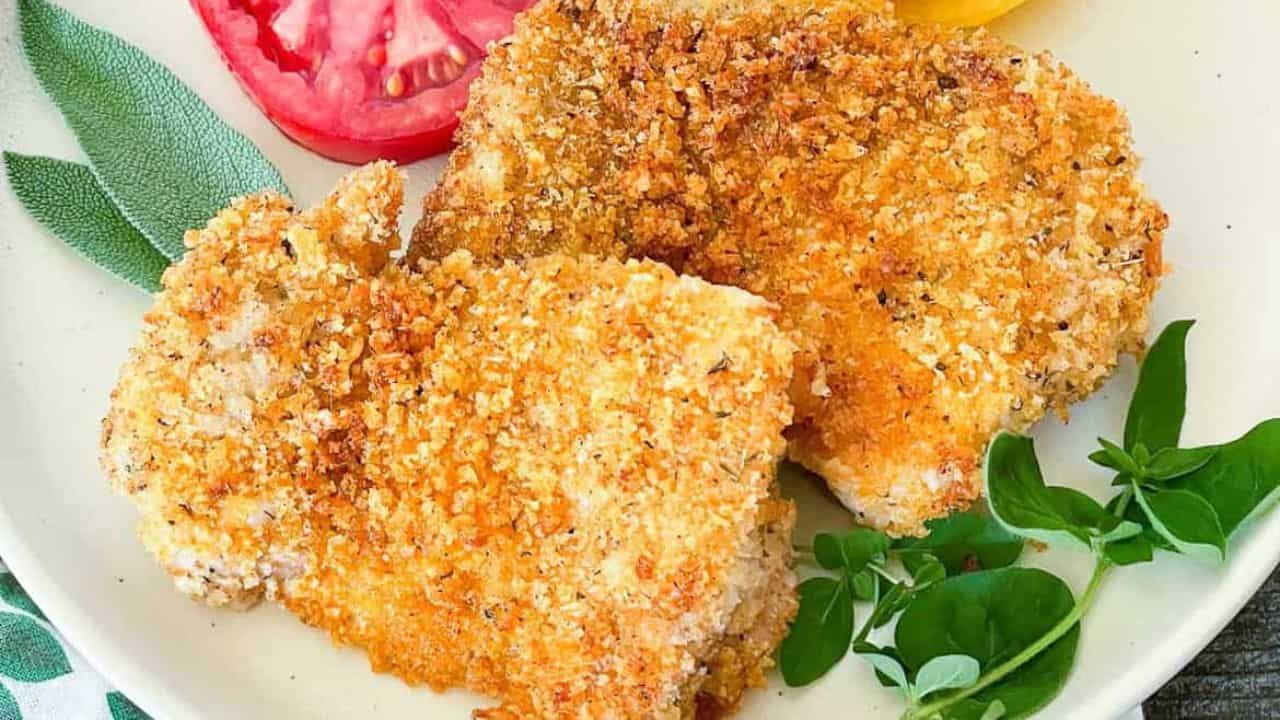 Panko chicken on a plate with tomato slices and fresh herbs.
