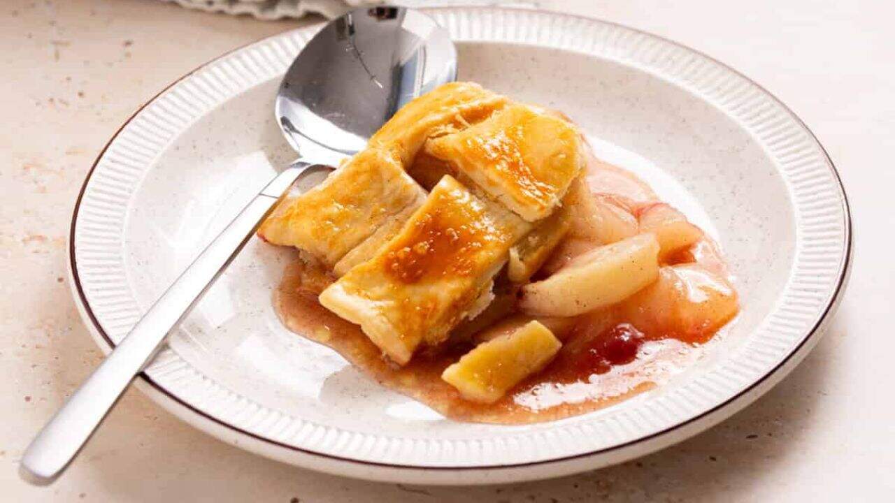 An image of peach cobbler in a baking dish with a portion of it missing.