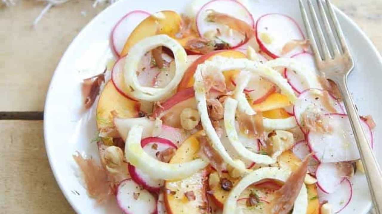 Peach radish salad with crispy prosciutto on a white plate with a fork.