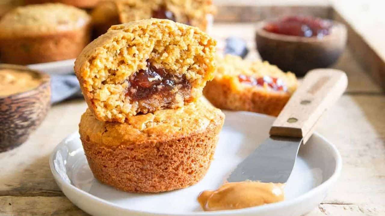 Peanut butter and jelly muffins on a plate with a spatula with peanut butter.