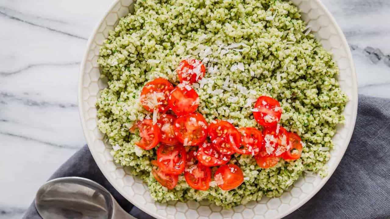 A bowl of pesto couscous with tomatoes and basil.