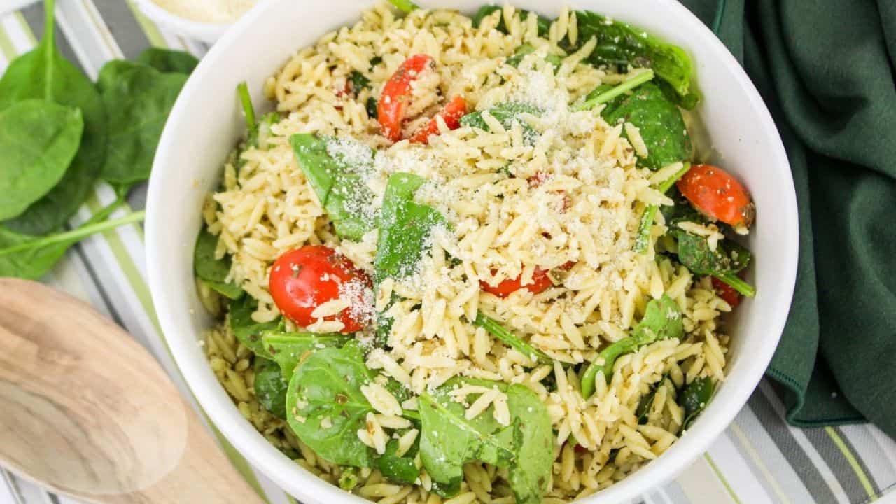 A bowl of orzo salad with spinach, cherry tomatoes, and grated cheese on top.