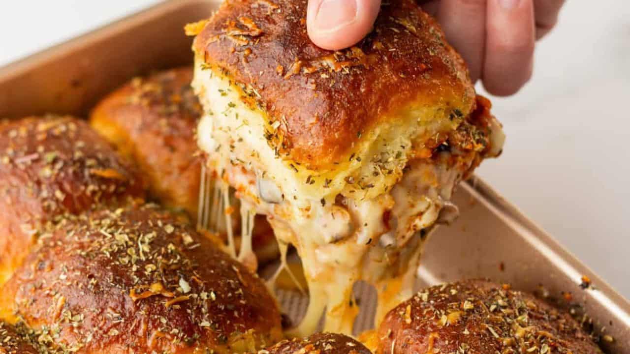 An image of a hand picking up one pizza slider from the baking pan.