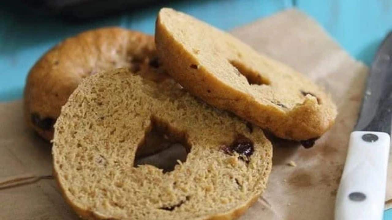 Three pumpkin raisin bagels stacked on a baking sheet dusted with cornmeal.