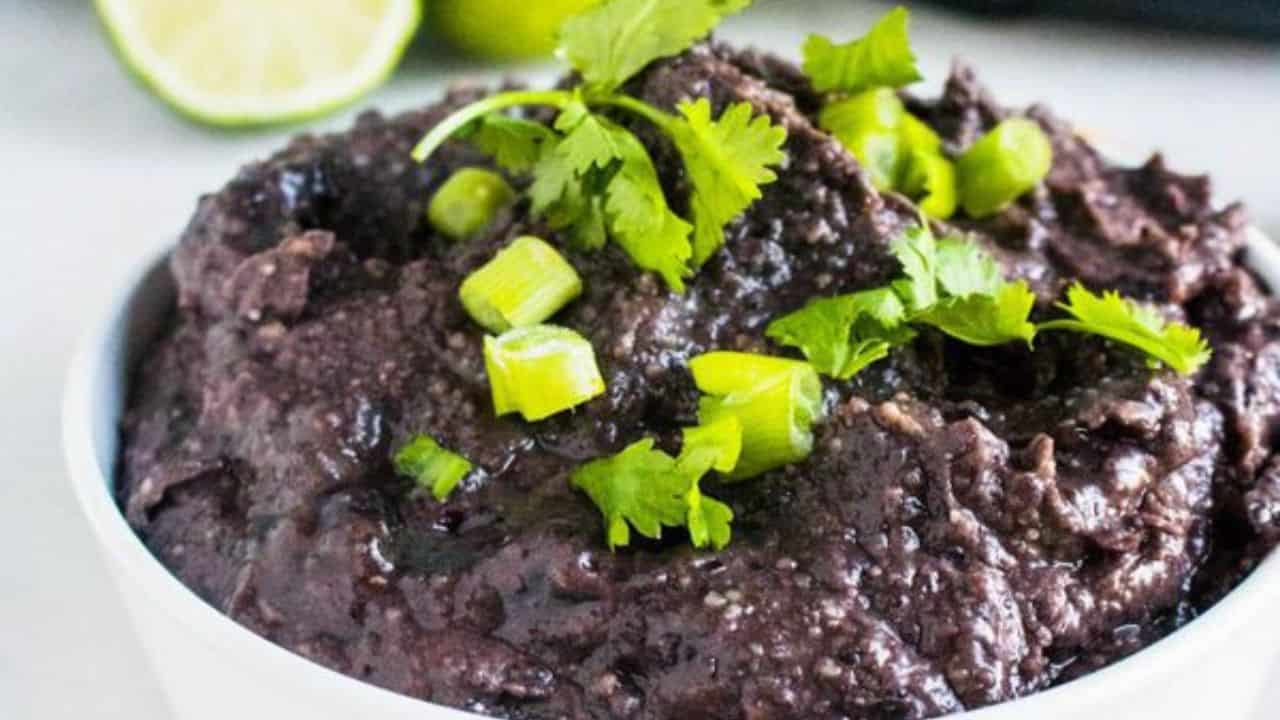 A bowl of black bean dip garnished with chopped green onions and fresh cilantro, with a lime wedge in the background.