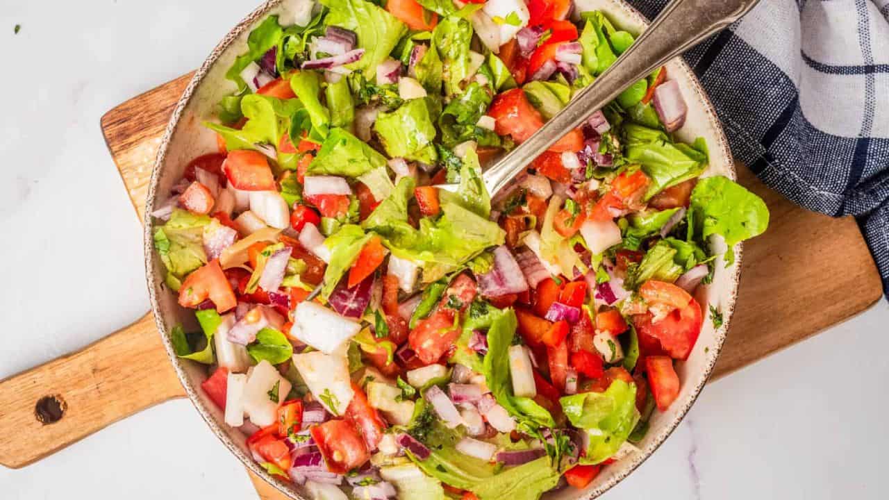 An overhead image of vegan chopped salad in a bowl with a serving spoon in the middle.
