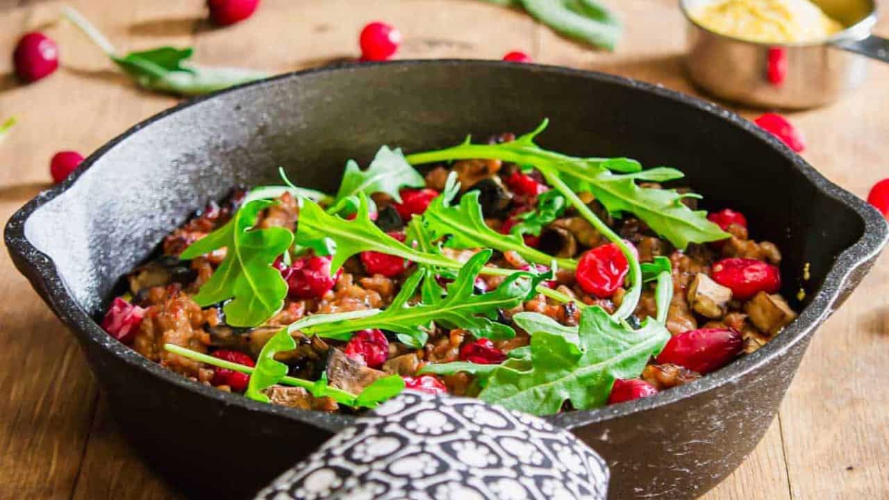 A serving spoon in a cast iron skillet with polenta and sausage.