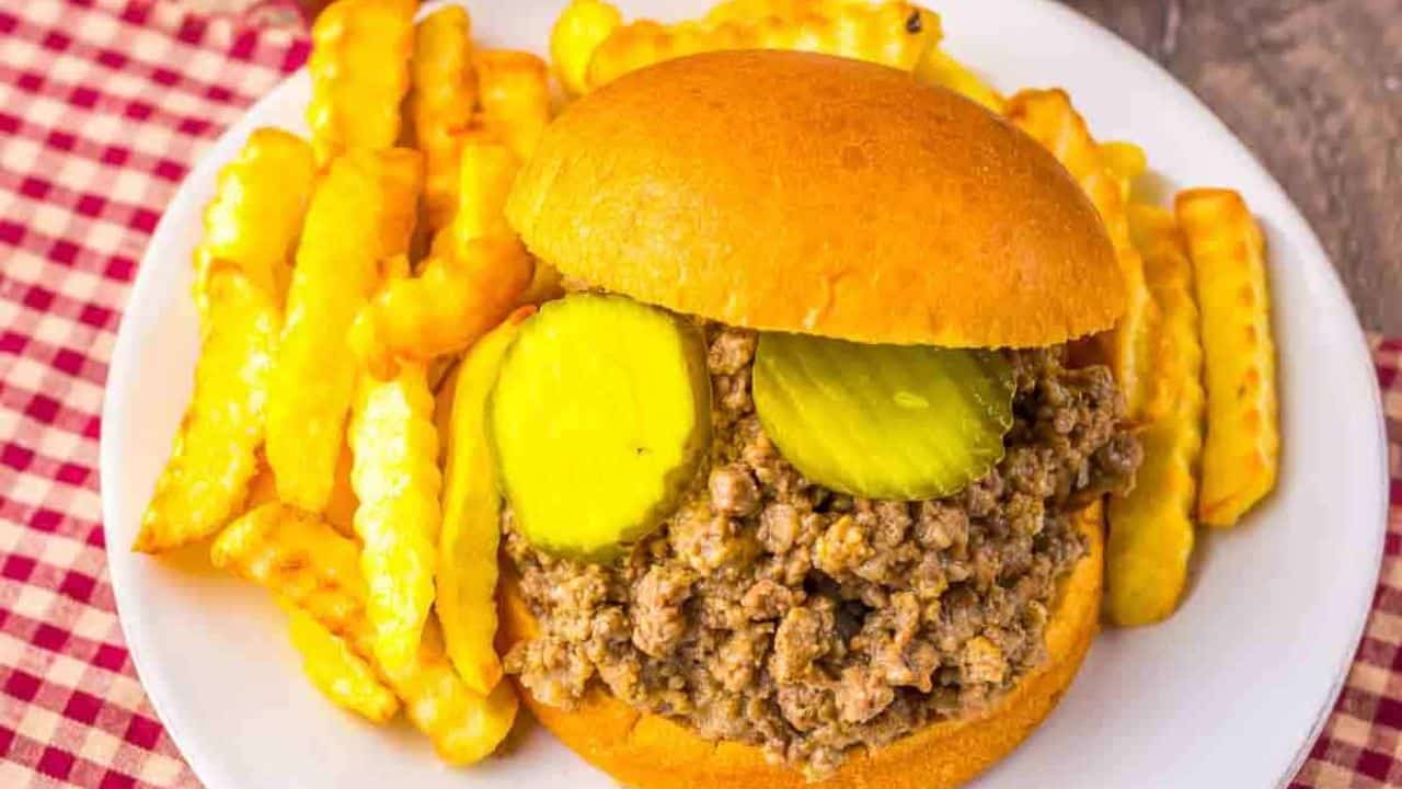 Slow cooker Maid-Rite sandwich with seasoned loose ground beef and pickles on a bun, served with crinkle-cut fries.