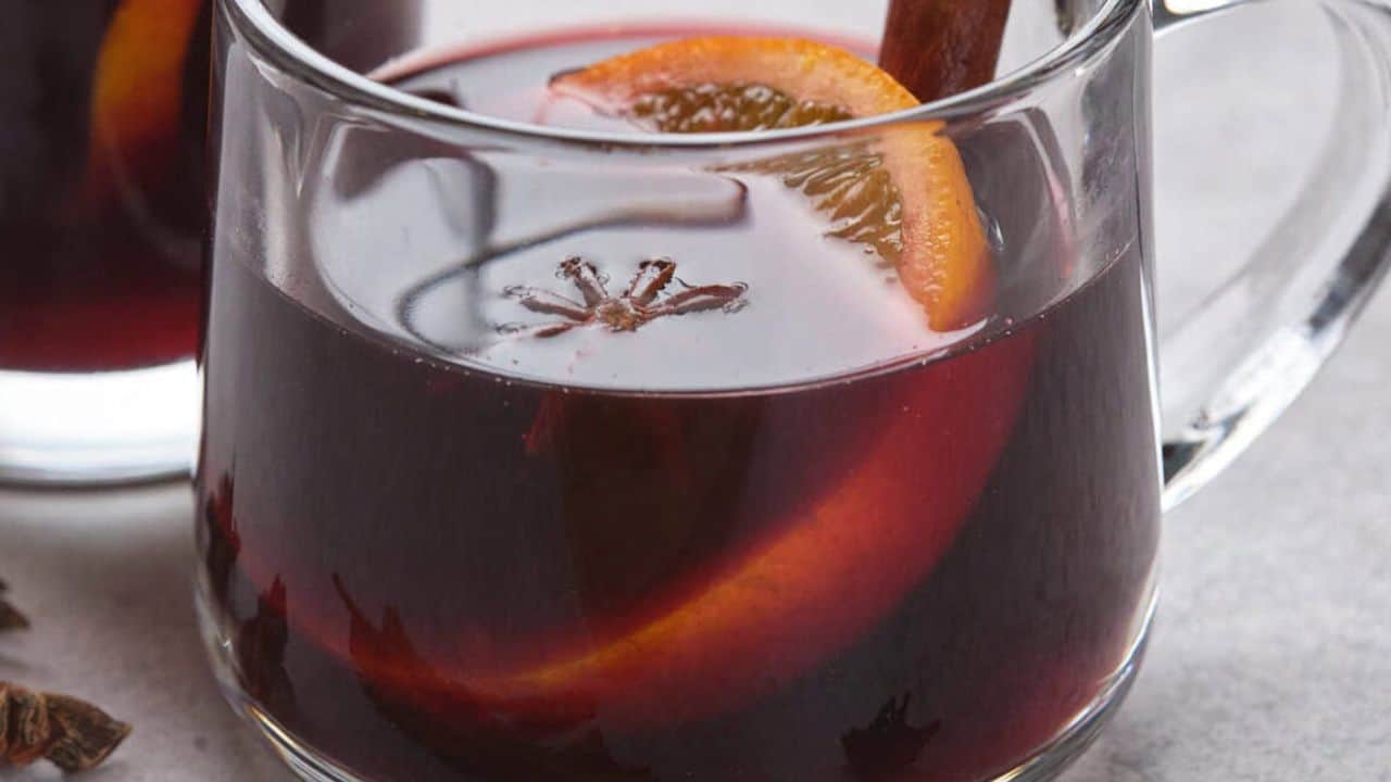 A clear glass mug filled with mulled wine, garnished with an orange slice, a cinnamon stick, and a star anise pod.