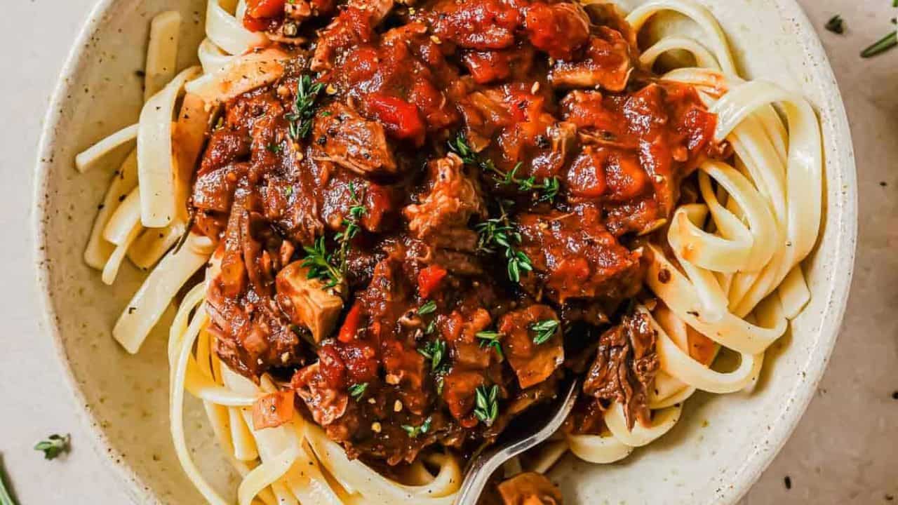 Slow cooker short rib ragu in a bowl over mashed sweet potatoes with a fork.