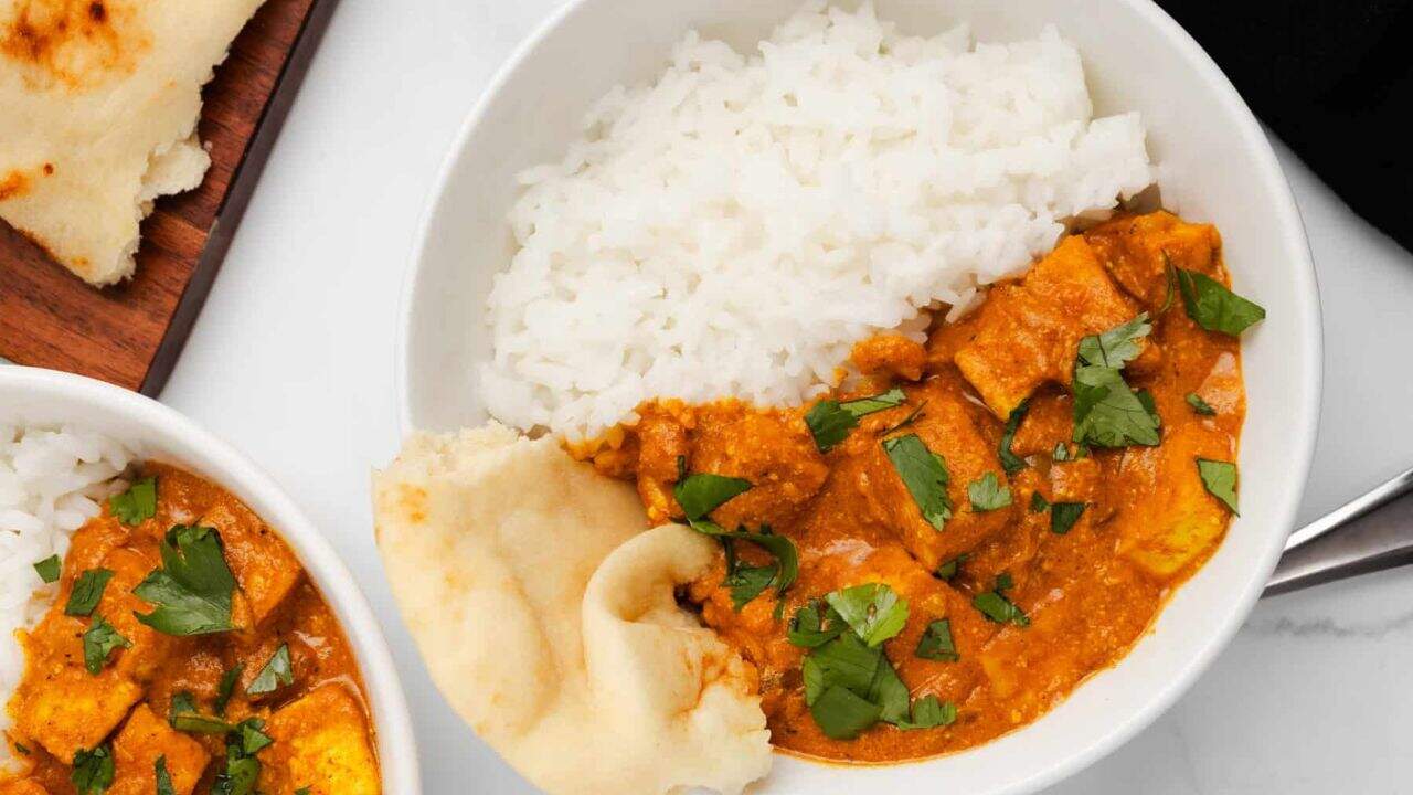 An overhead image of slow cooker tikka masala in a bowl with rice, with a slow cooker on the background.