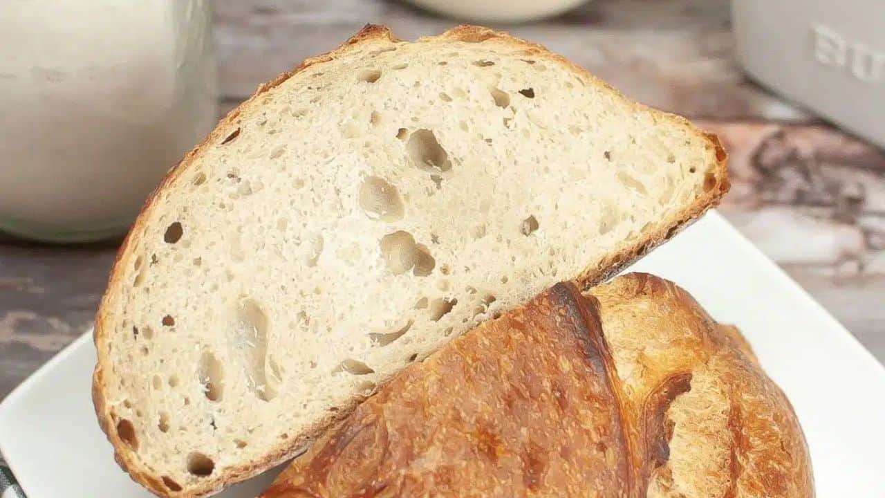 Two slices of rustic bread on a white plate, next to a checkered cloth and a butter container on a wooden surface.