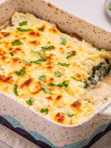 Baked casserole with a golden, cheesy topping and green herbs, shown in a rectangular ceramic dish on a white towel.