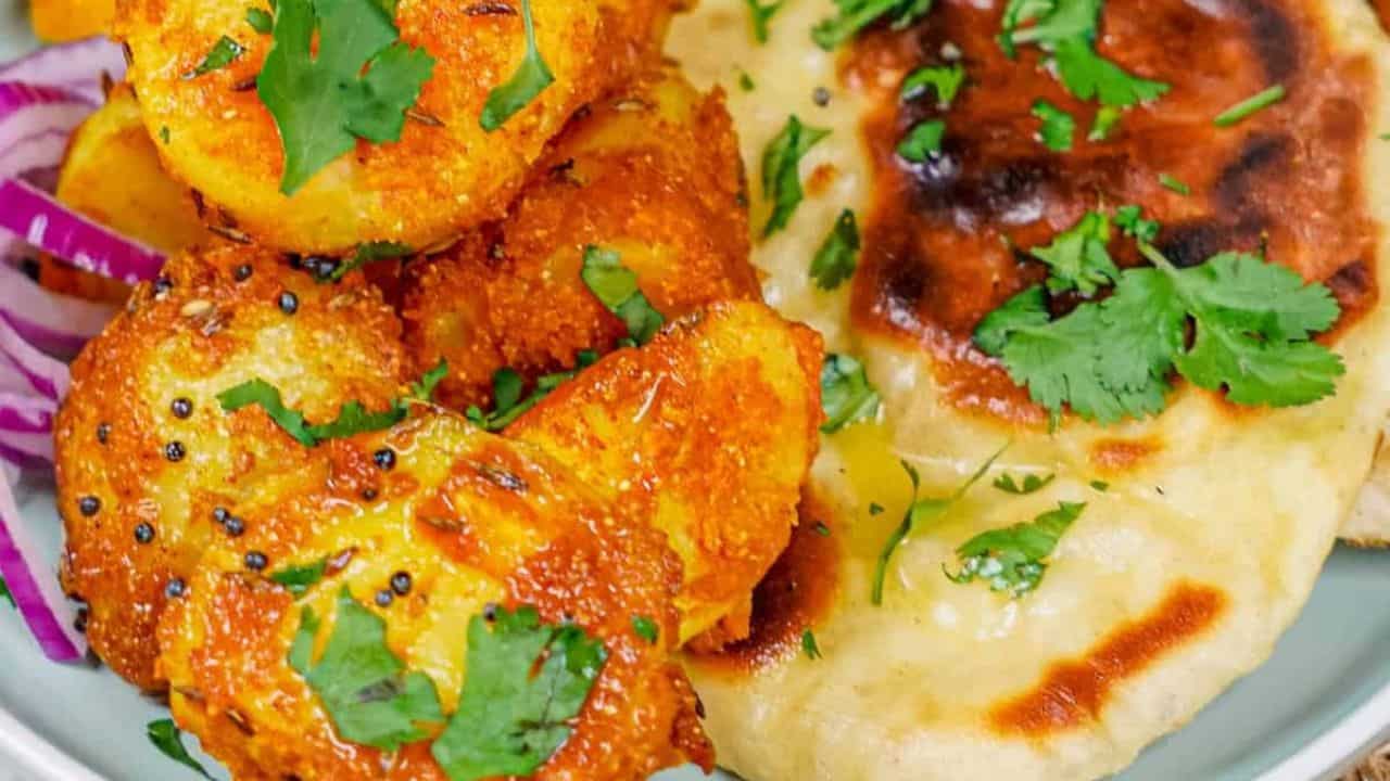 Horizontal shot of Bombay Potatoes on a plate with naan, with extra naan and red onions on the side.
