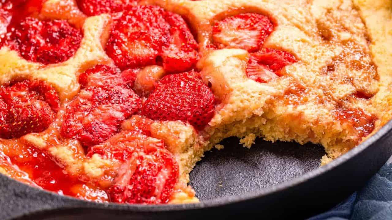 A close up shot of strawberry spoon cake in a cast iron skillet, ready to be served.